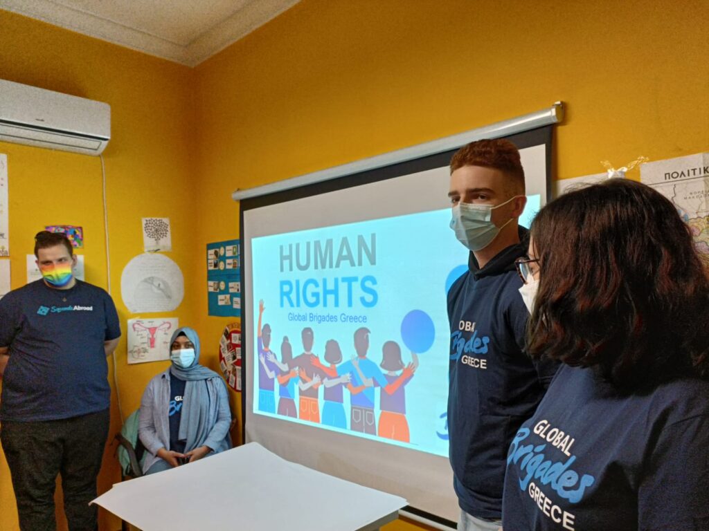 Emmanuel and classmates in front of a PowerPoint slide reading “Human Rights. Global Brigades Greece.”